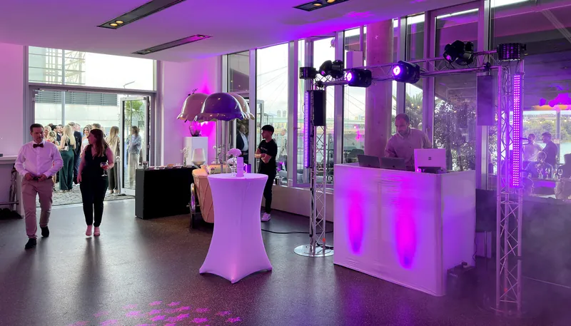 DJ hinter weißem Pult mit violettem Licht in einer verglasten Eventlocation