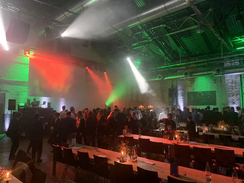 Tanzende Gäste vor dem DJ-Bereich mit Lichtstrahlen in einer großen Veranstaltungshalle