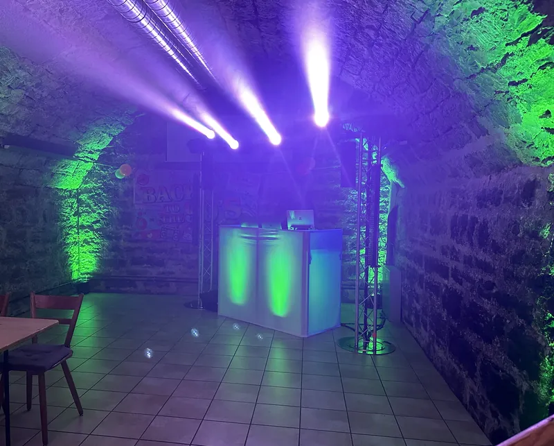 DJ-Aufbau im Gewölbekeller mit grüner Beleuchtung und violetten Lichtstrahlen