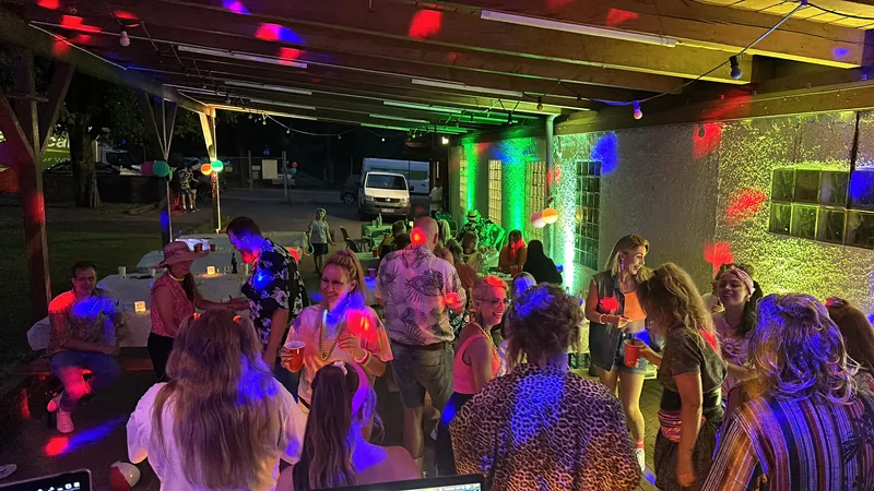 Feiernde Gäste unter einem Holzdach bei bunter Partybeleuchtung
